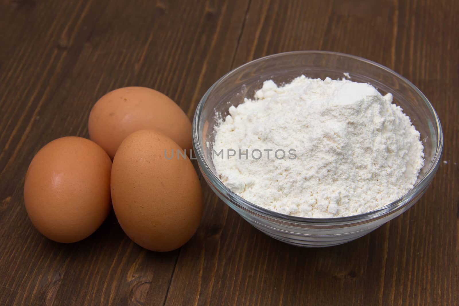 Eggs and flour in bowl on wooden table