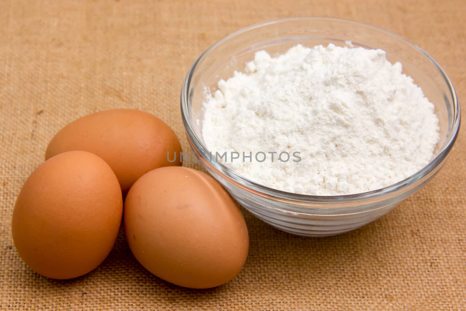 Eggs and flour in bowl on jute cloth
