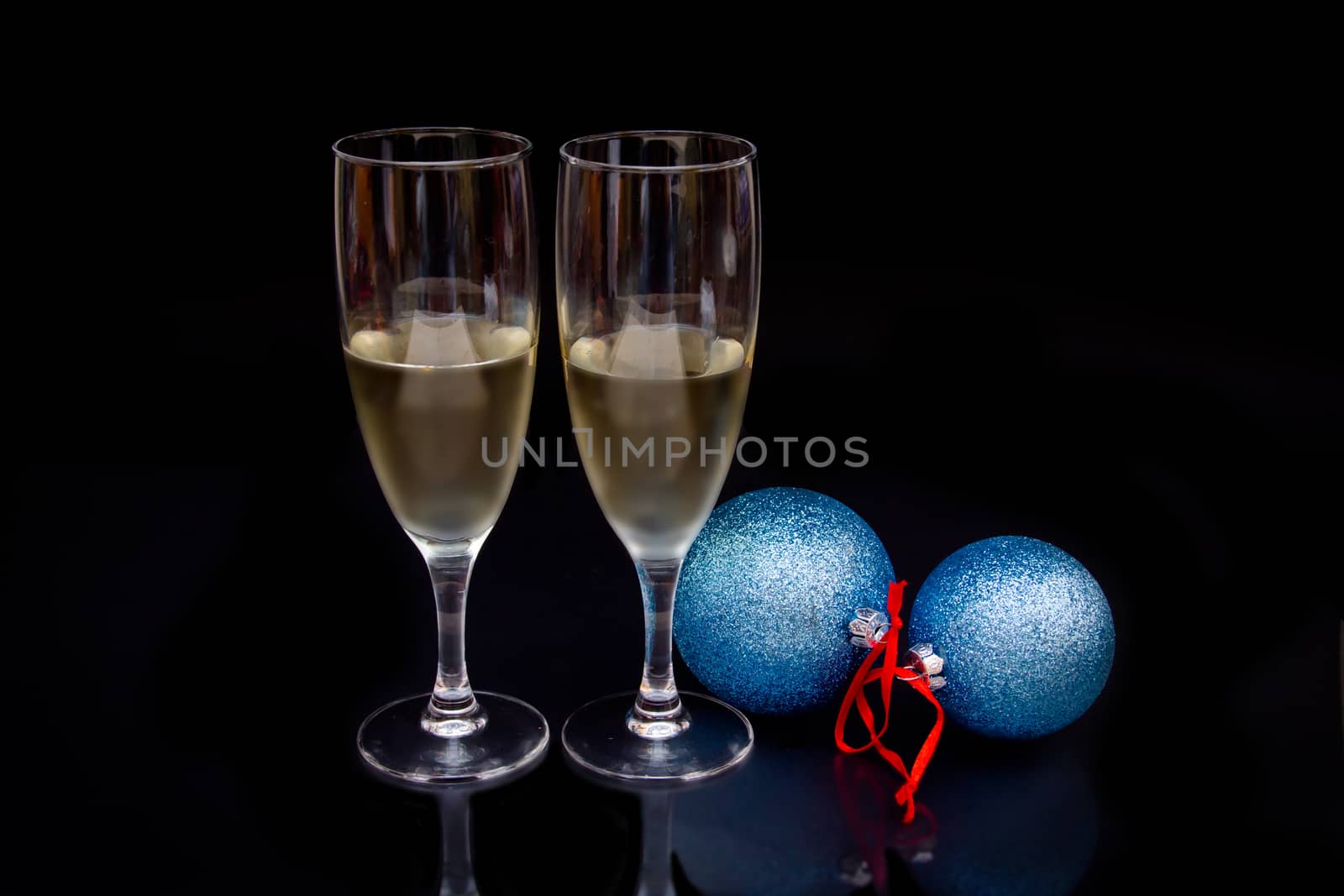 Flute with sparkling and christmas balls which are reflected on a black background