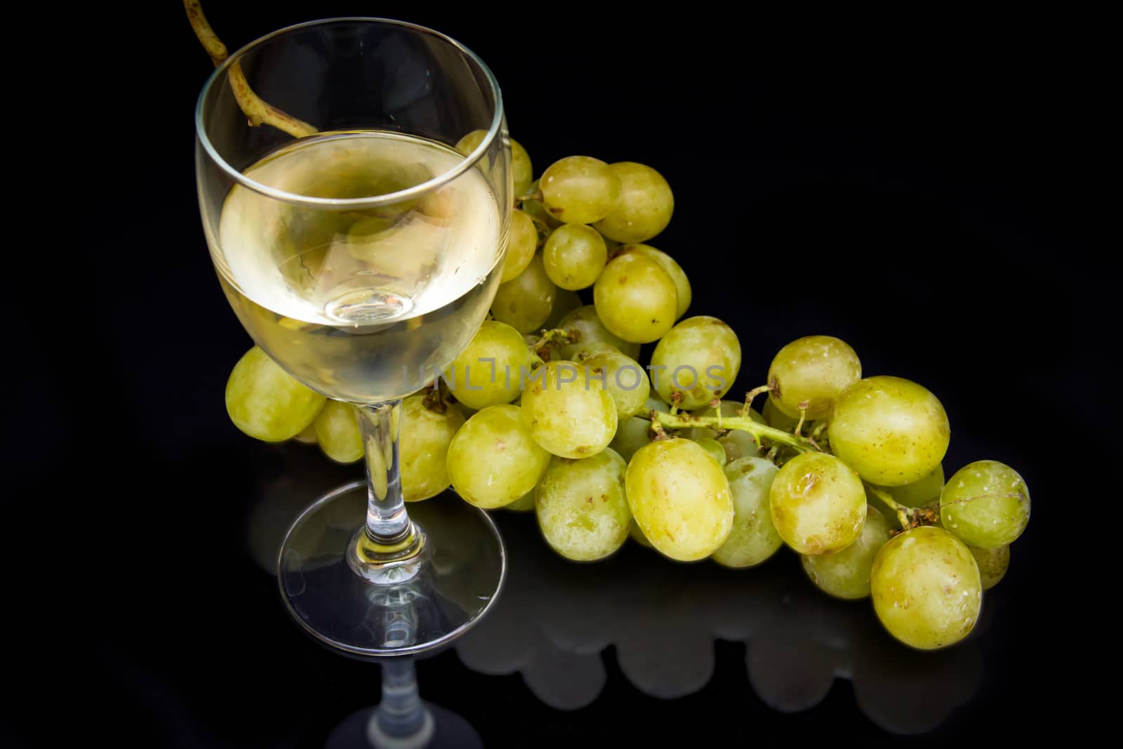 Wine glass with a bunch of grapes reflected on black background