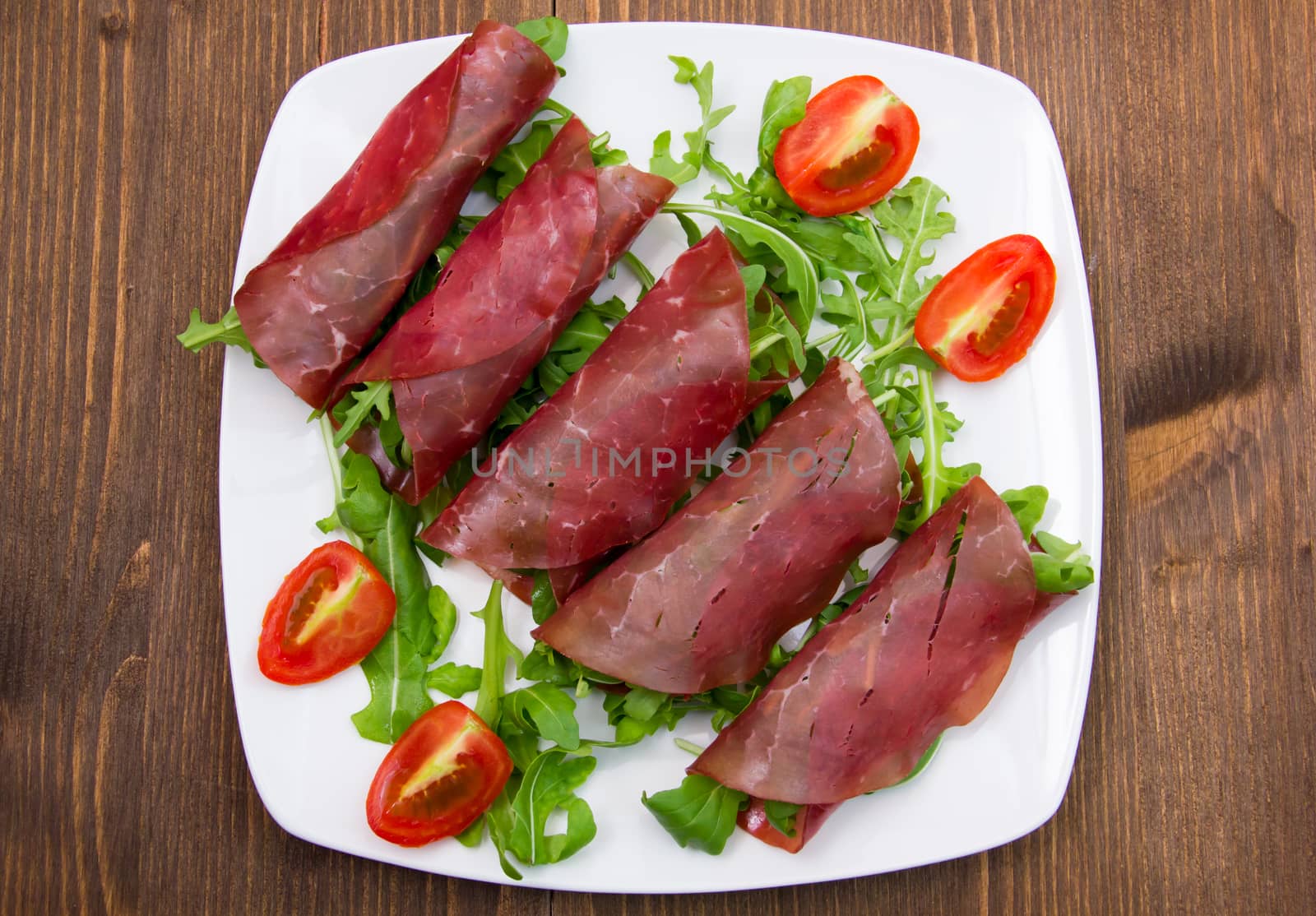 Rolls of dried beef on plate over wooden table seen from above