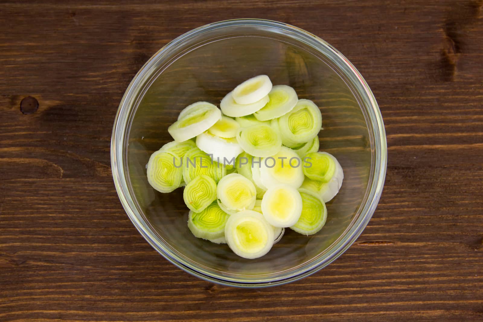 Bowl with sliced leek on wooden table seen from above