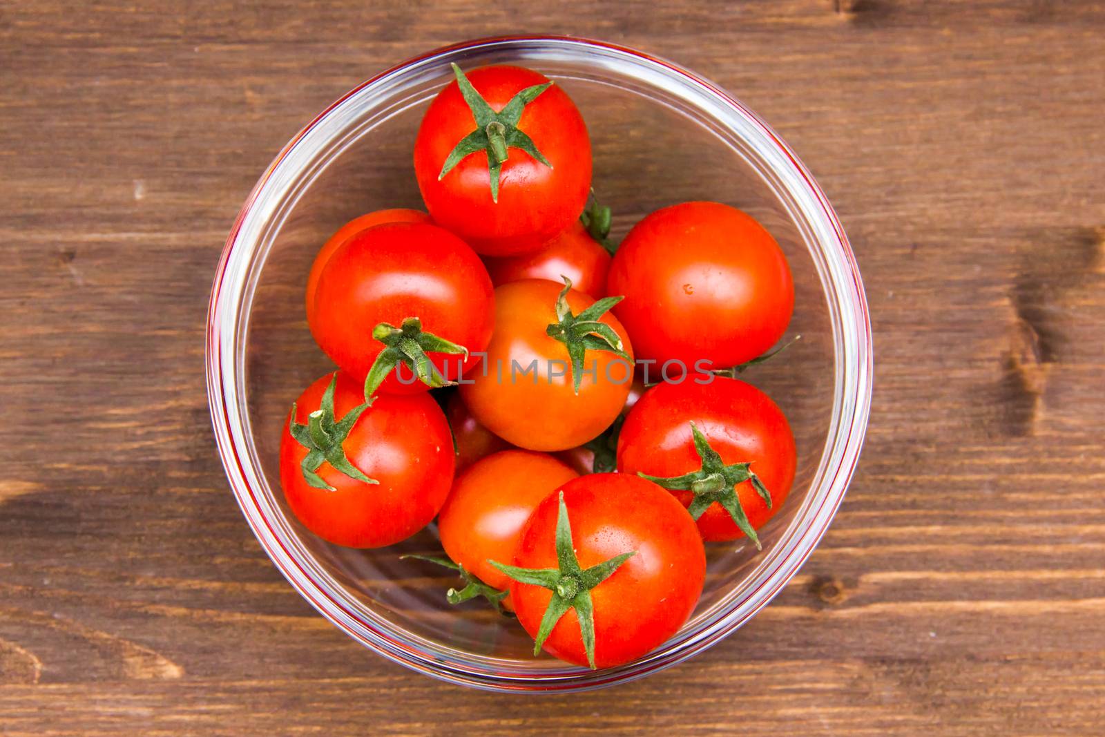 Glass bowl with tomatoes on wooden seen from above