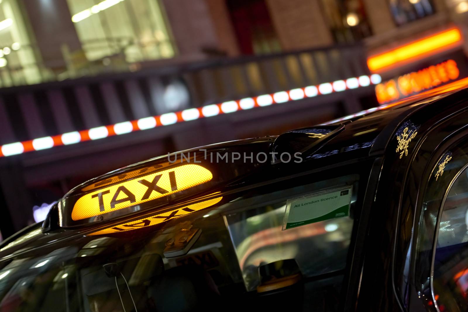 Low key detail of London black cab sign turned on at night, with shop lights in the background.