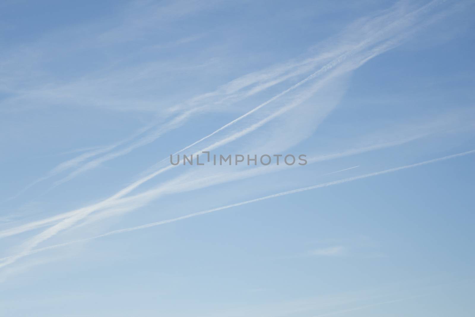 Blue sky with gray white clouds shot from airplane window in flight flying over the clouds on winter day with vapor trails.