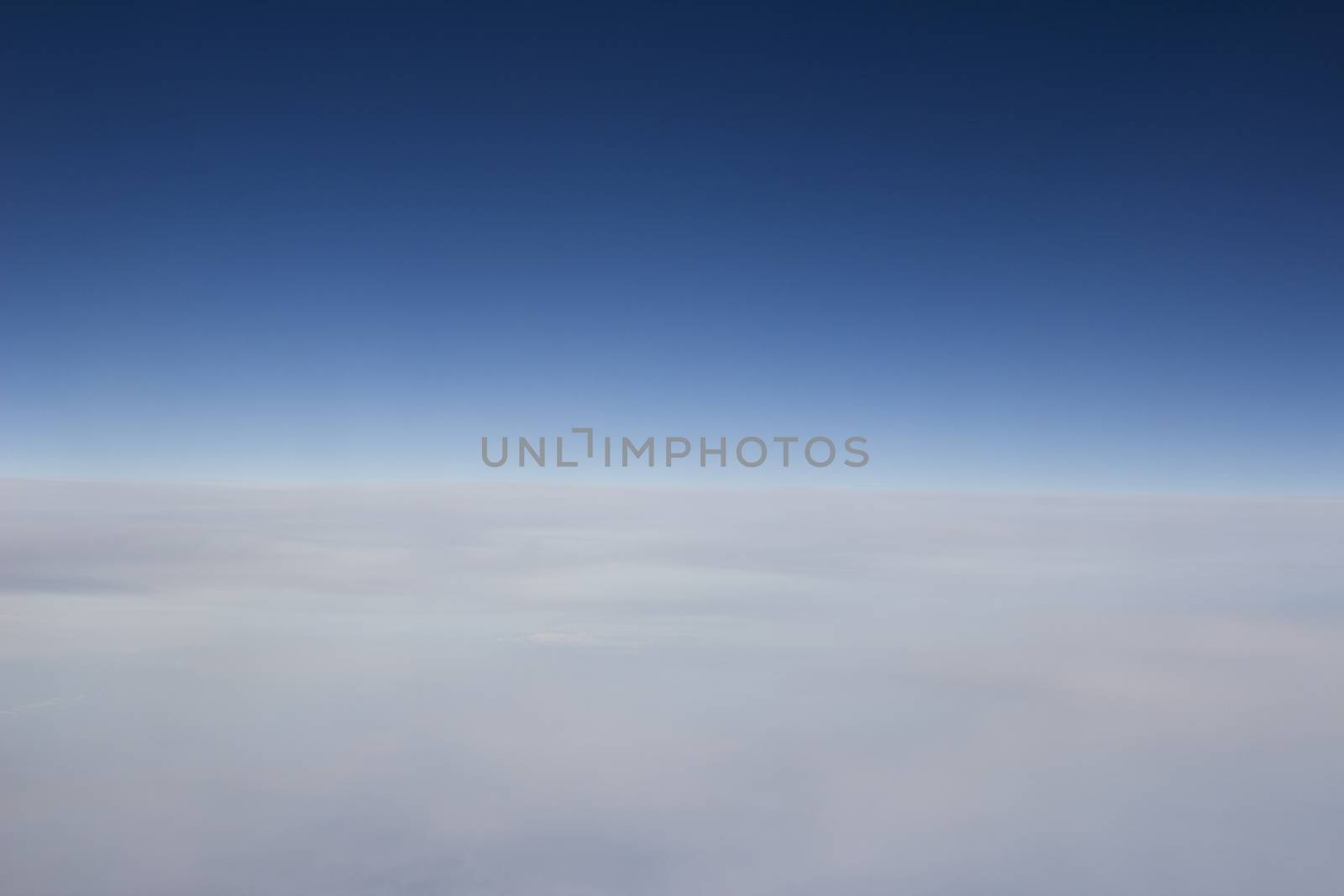 Blue sky with gray white clouds shot from airplane window in flight flying over the clouds on winter day.