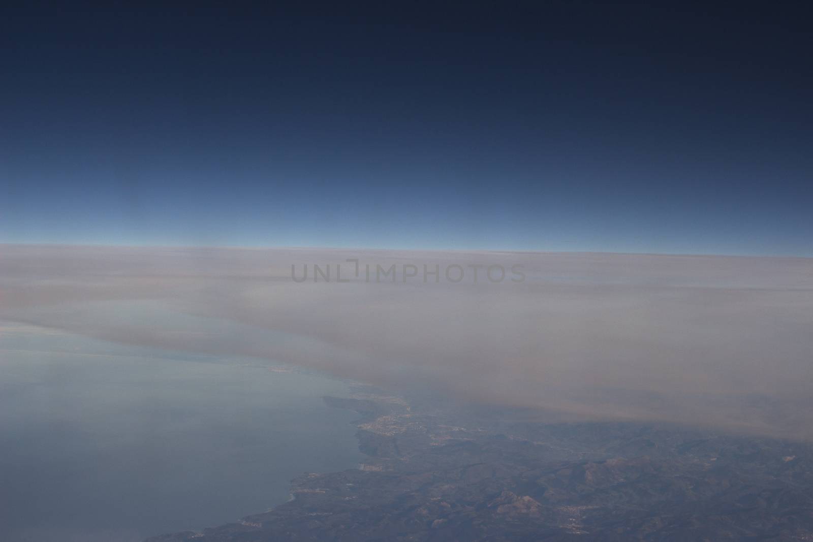 Blue sky with gray white clouds and ground shot from airplane window in flight flying over the clouds on winter day.