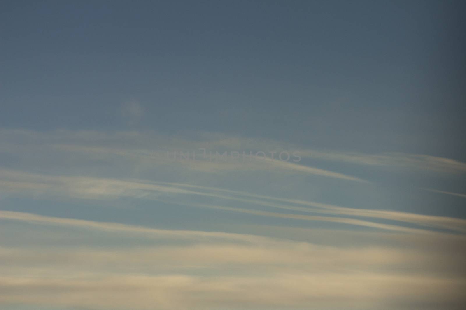 Blue sky with gray white clouds shot from airplane window in flight flying over the clouds on winter day.