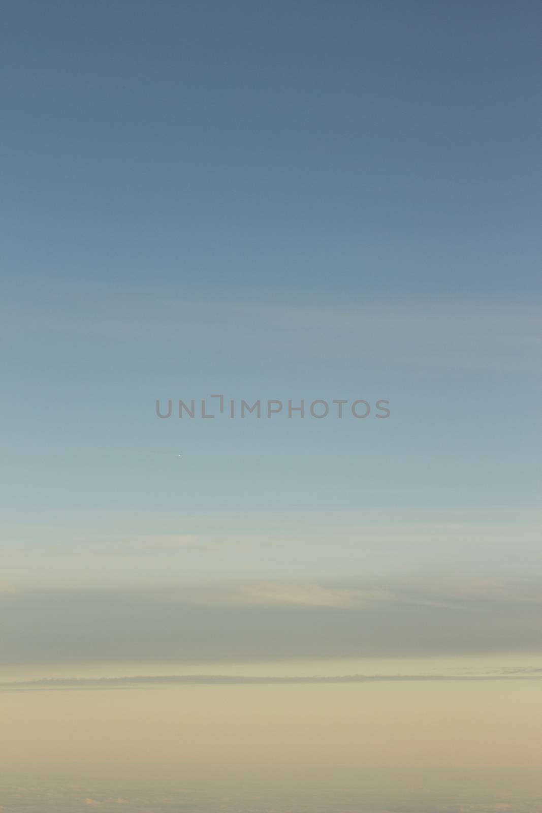 Blue sky with gray white clouds shot from airplane window in flight flying over the clouds on winter day.