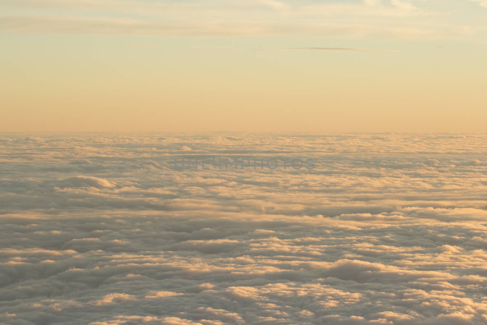 Sky with clouds in blue and pink purple sunset evening pastel colors photo shot from an airplane in flight flying above the cloud level.