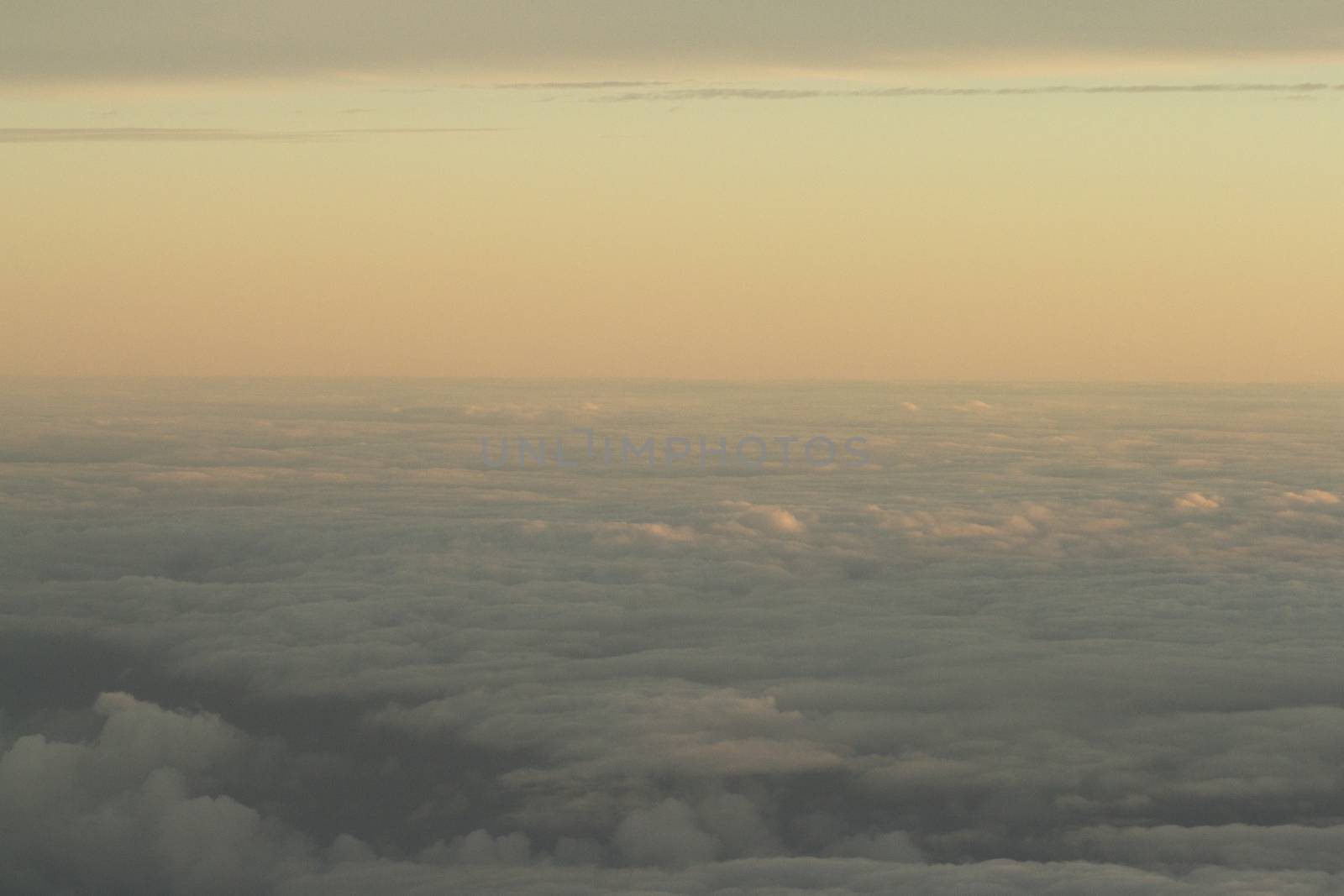Sky with clouds in blue and pink purple sunset evening pastel colors photo shot from an airplane in flight flying above the cloud level.
