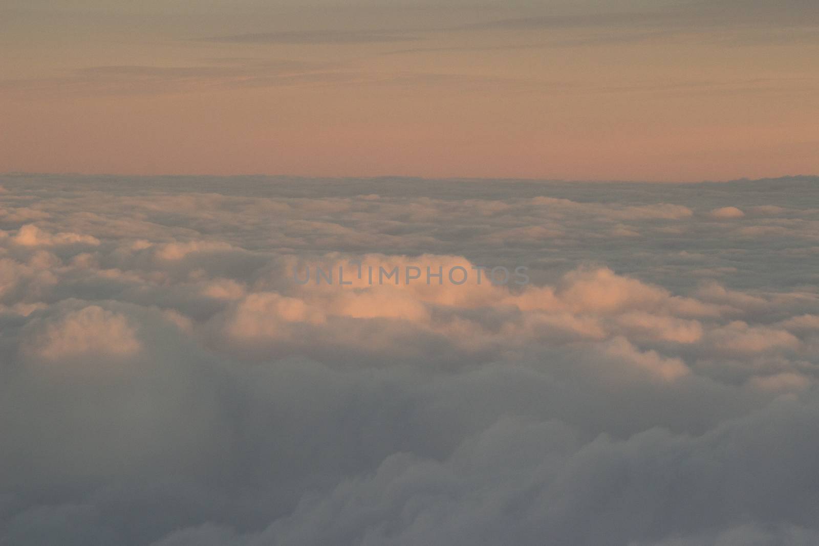 Sky with clouds in blue and pink purple sunset evening pastel colors photo shot from an airplane in flight flying above the cloud level.