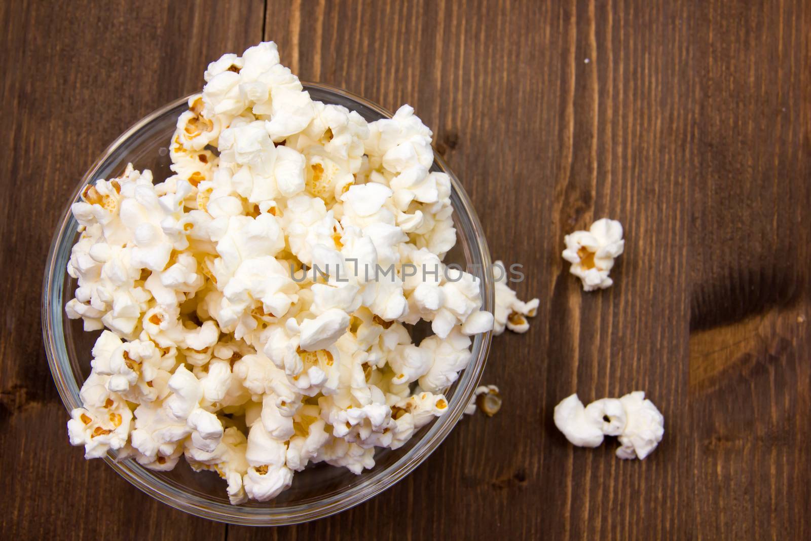 Popcorn in bowl on wooden table seen from above