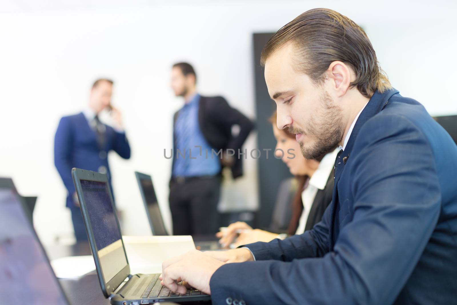 Businessman working on laptop during the meeting. Workplace in modern office with business people meeting in the background.