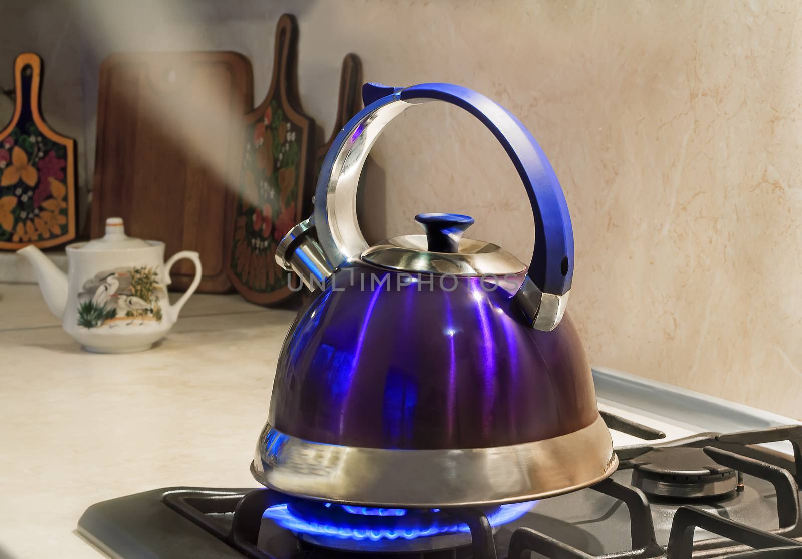 Blue kettle with a signal of boiling water and steam jet from the spout is on the burning gas stove