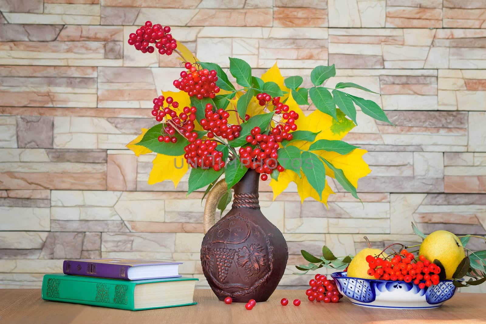 Autumn yellow leaves and bright red berries in a ceramic jug. Near are Rowan berries. Autumn still life.