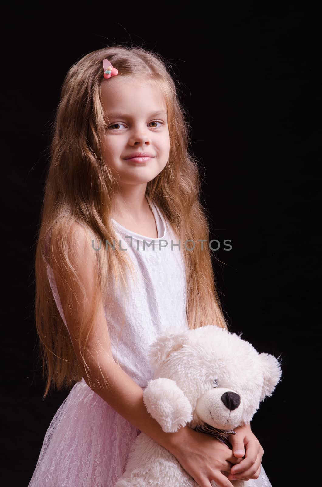 Portrait of a beautiful five year old girl with a teddy bear on a black background