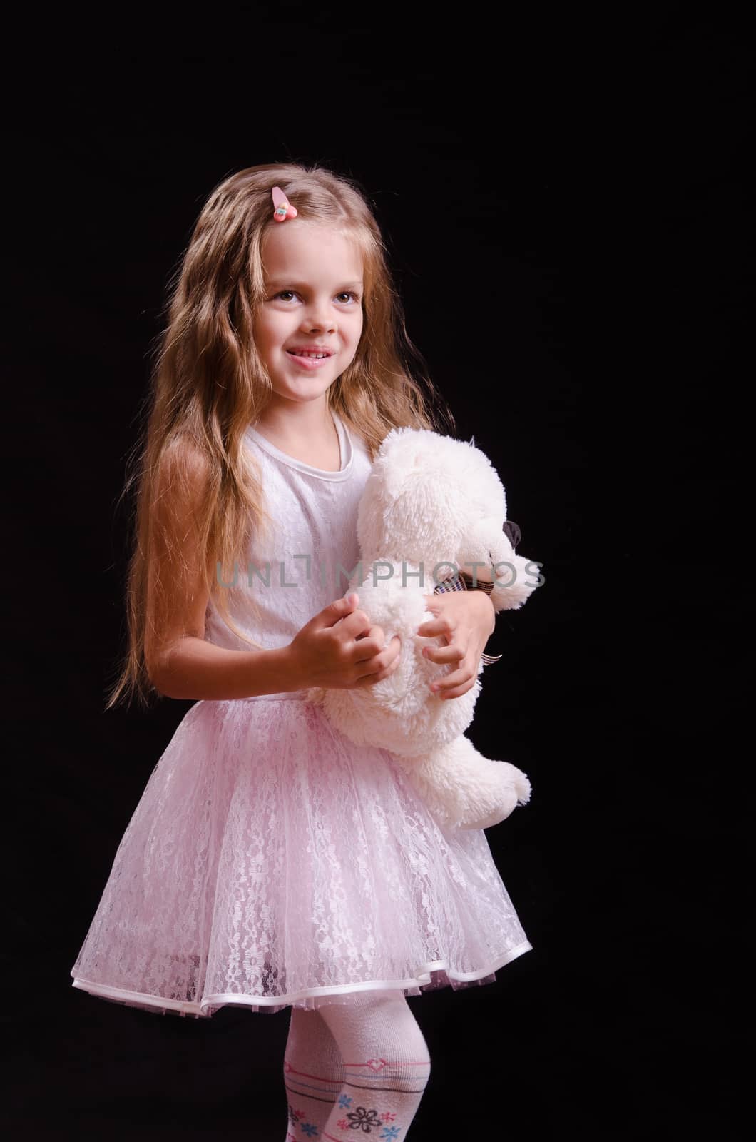 Portrait of a beautiful five year old girl with a teddy bear on a black background