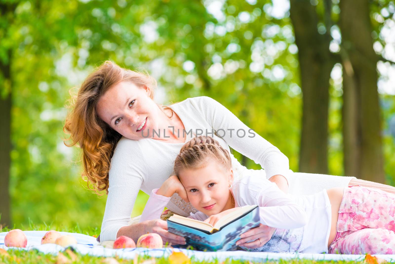 Mom and daughter reading a book lying in the park