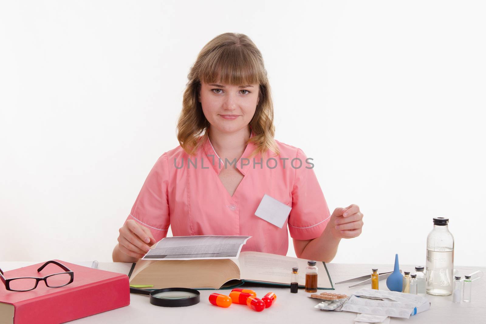 Pharmacist sitting at the table reading a thick handbook of medicines