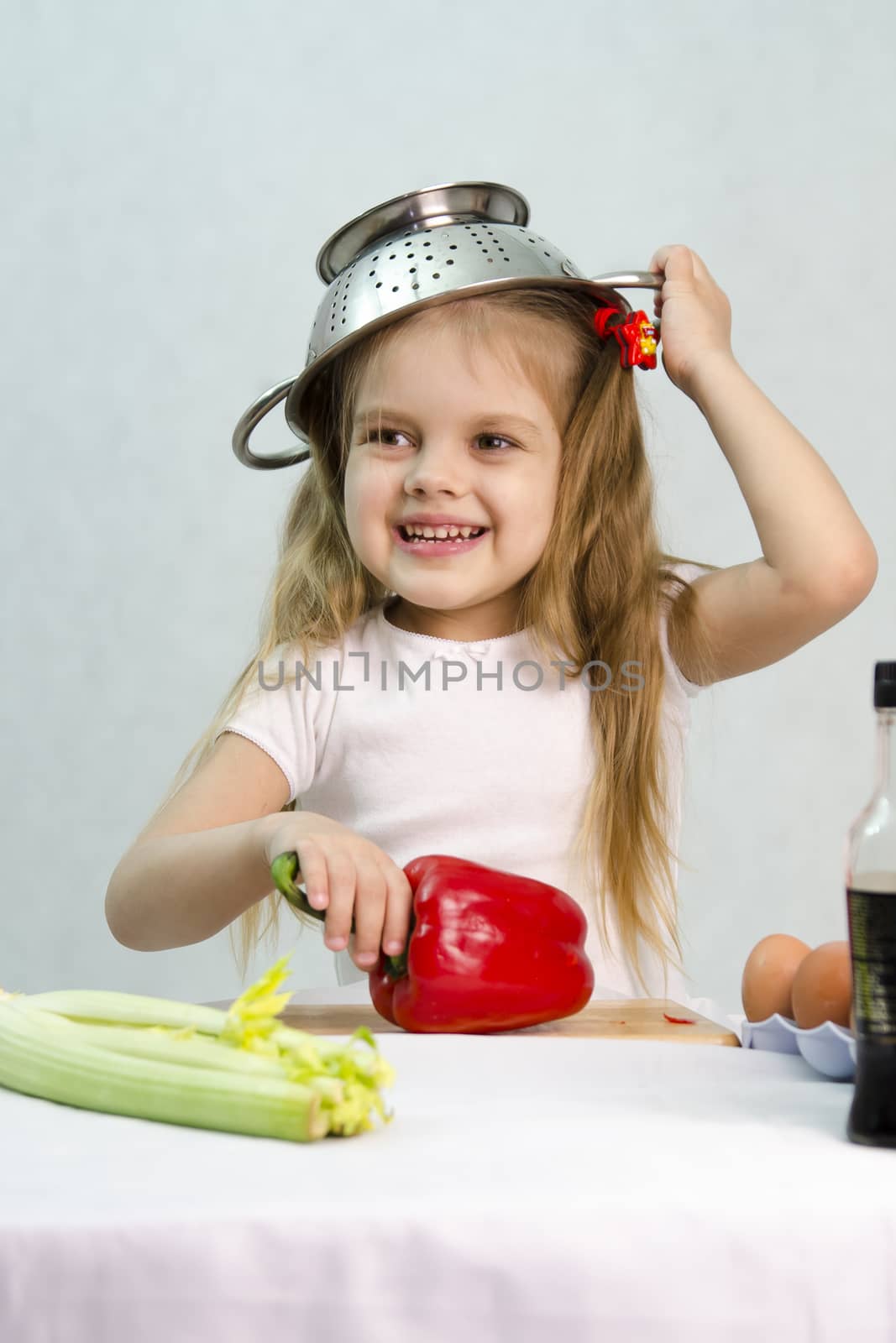 Girl playing in a cook. Carried away by the game she put on a colander on his head. Studio. Light background.