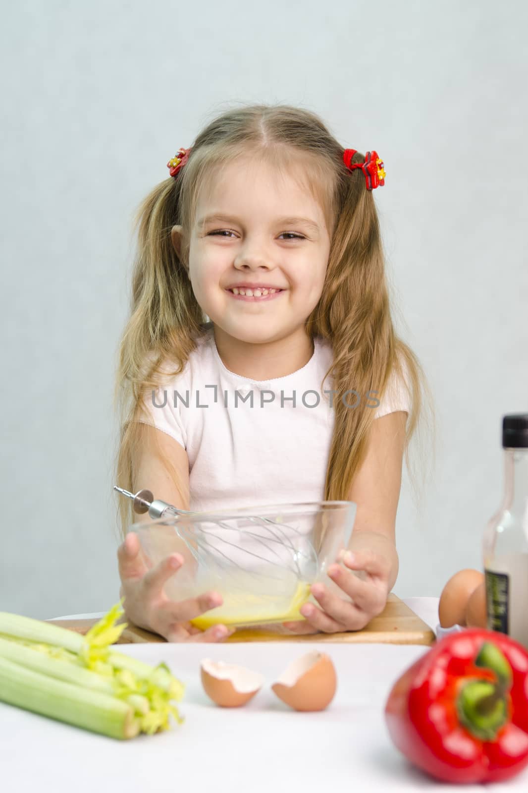 Girl playing in a cook. Girl churn whisk the eggs in a glass bowl. At the forefront of the shell, celery, pepper. Studio. Light background.