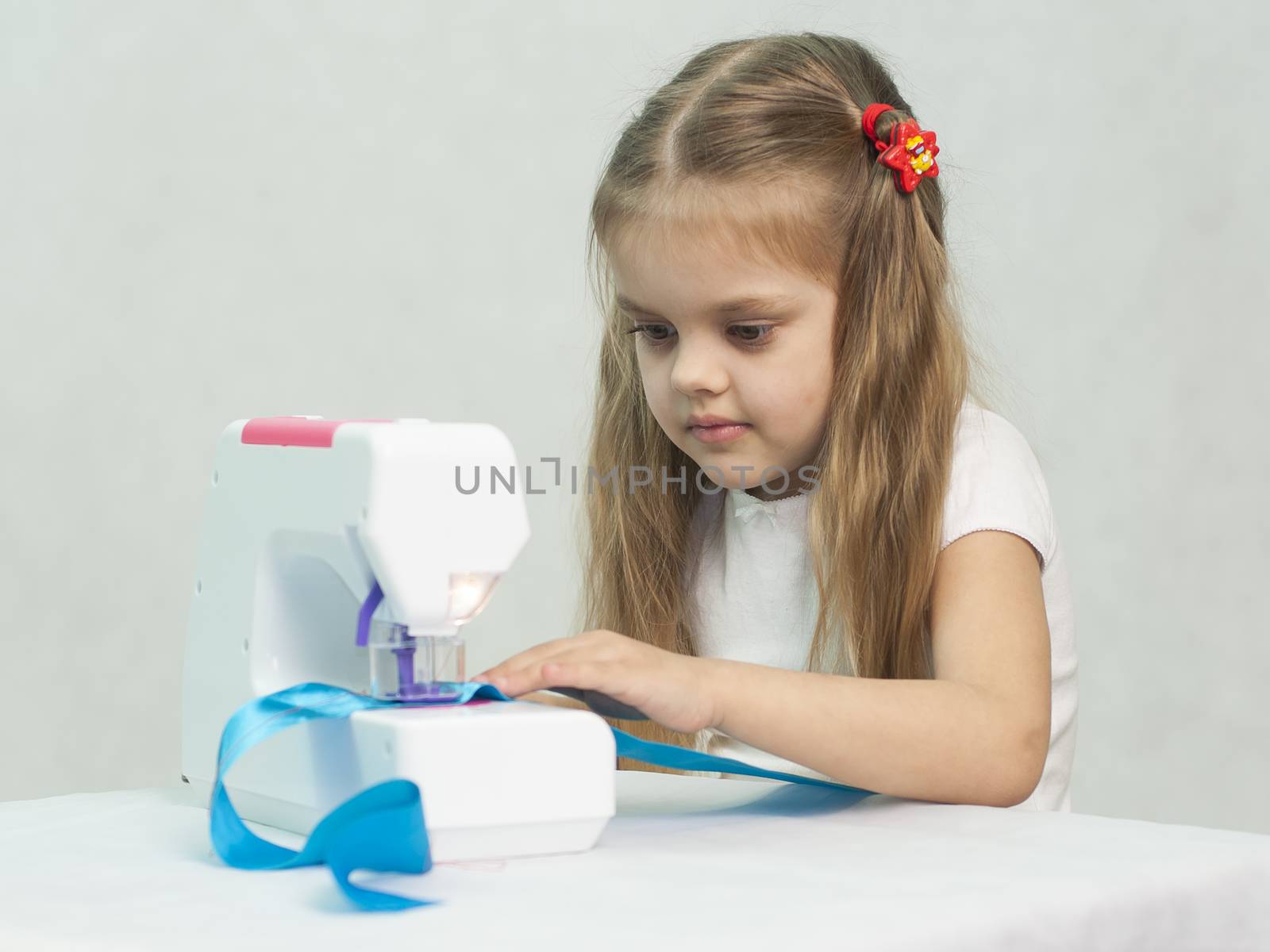 Girl sew on a children's sewing machine. Studio, a white background.