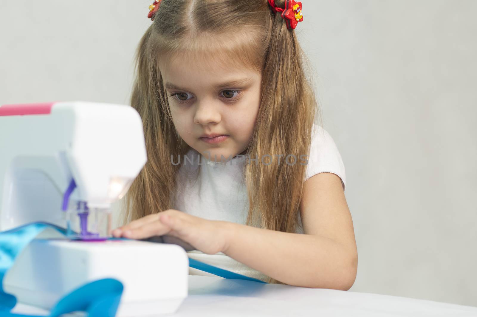 Girl sew on a children's sewing machine. Studio, a white background.
