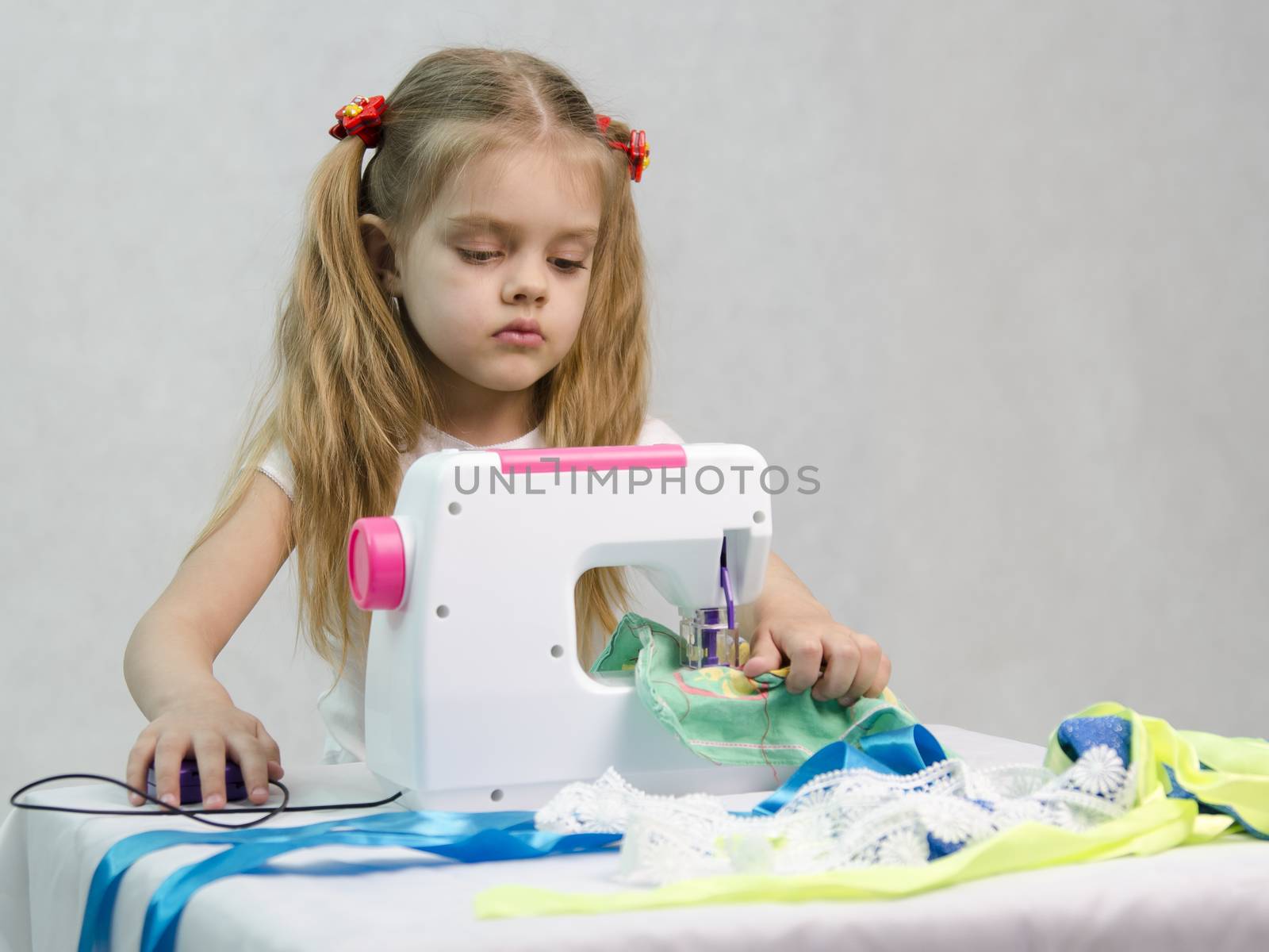 Girl sew on a children's sewing machine. Studio, a white background.