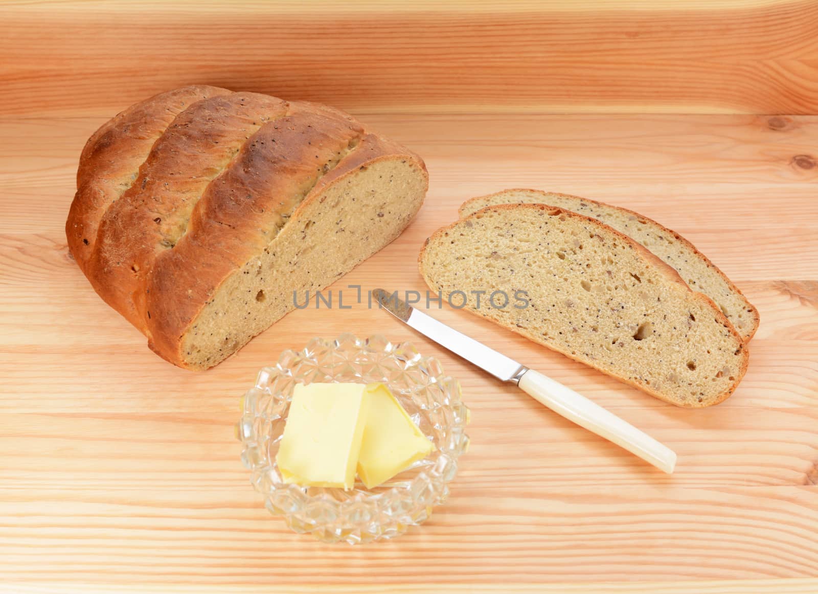 Slices of fresh bread with pats of butter and a small knife on a wooden table