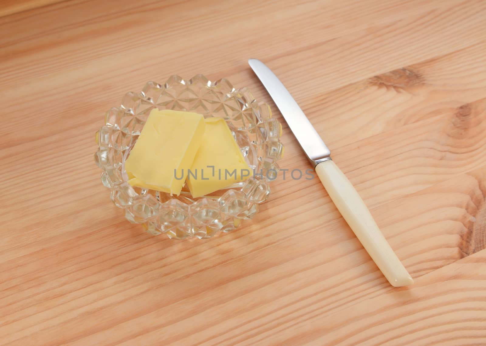 Butter in a glass dish with a small knife for spreading, on a pine wood table