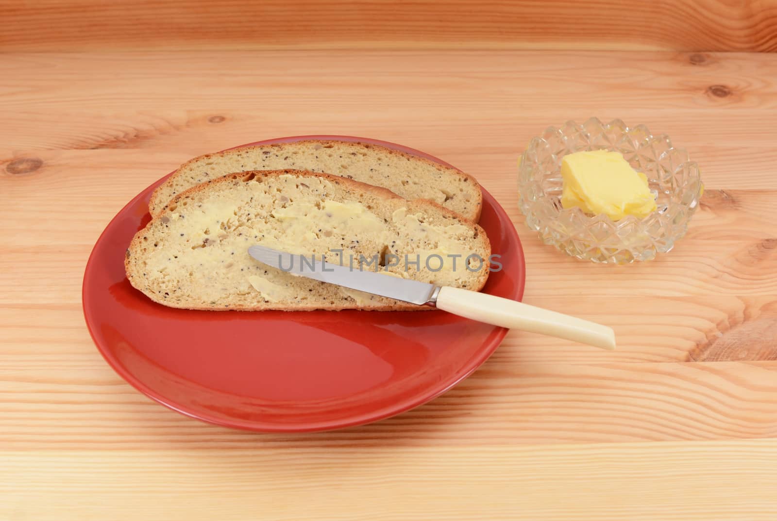 Buttered slices of bread on a red plate with a knife and butter dish