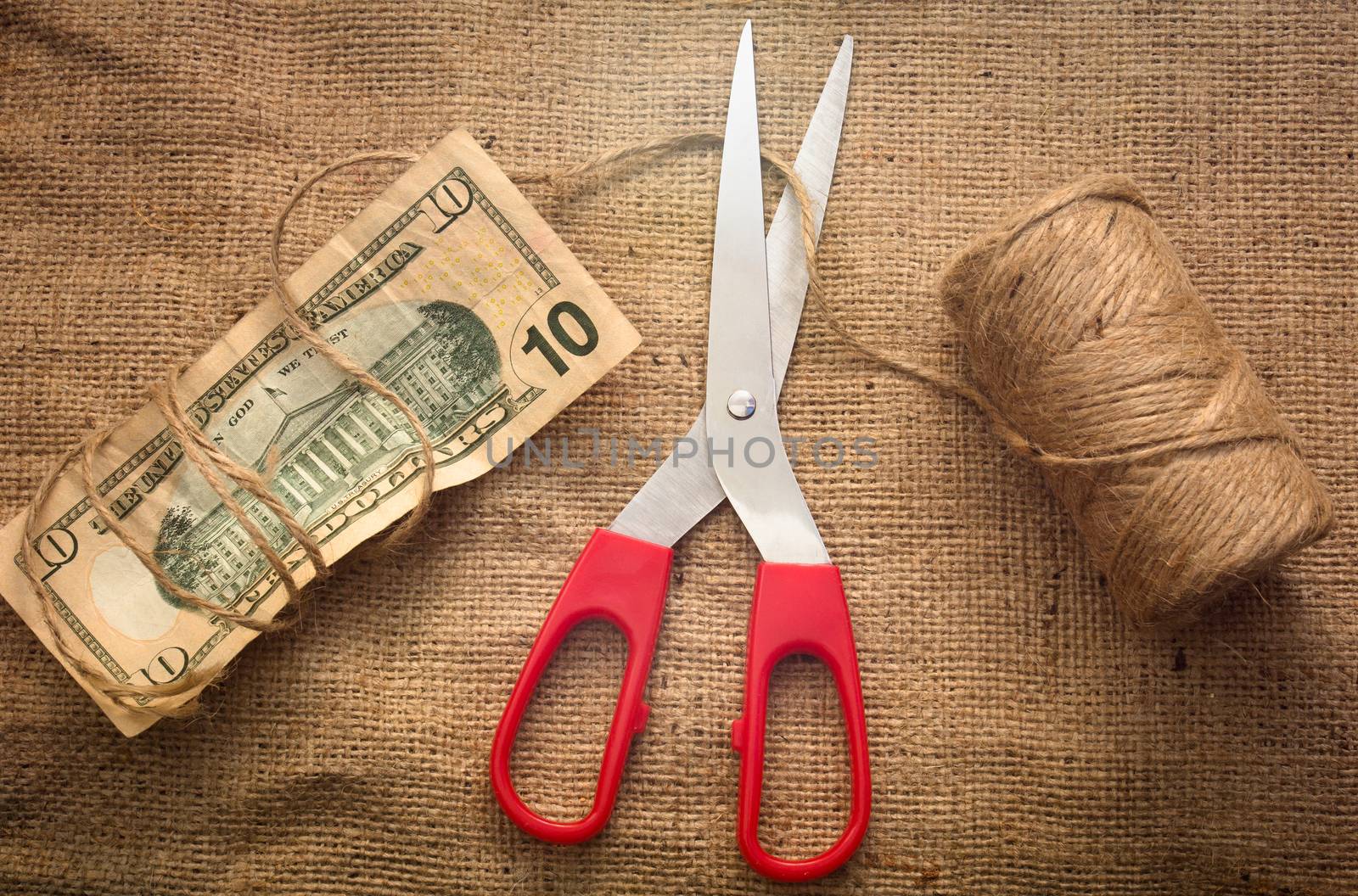 A scissor cutting a rope holding a 10 dollar bill