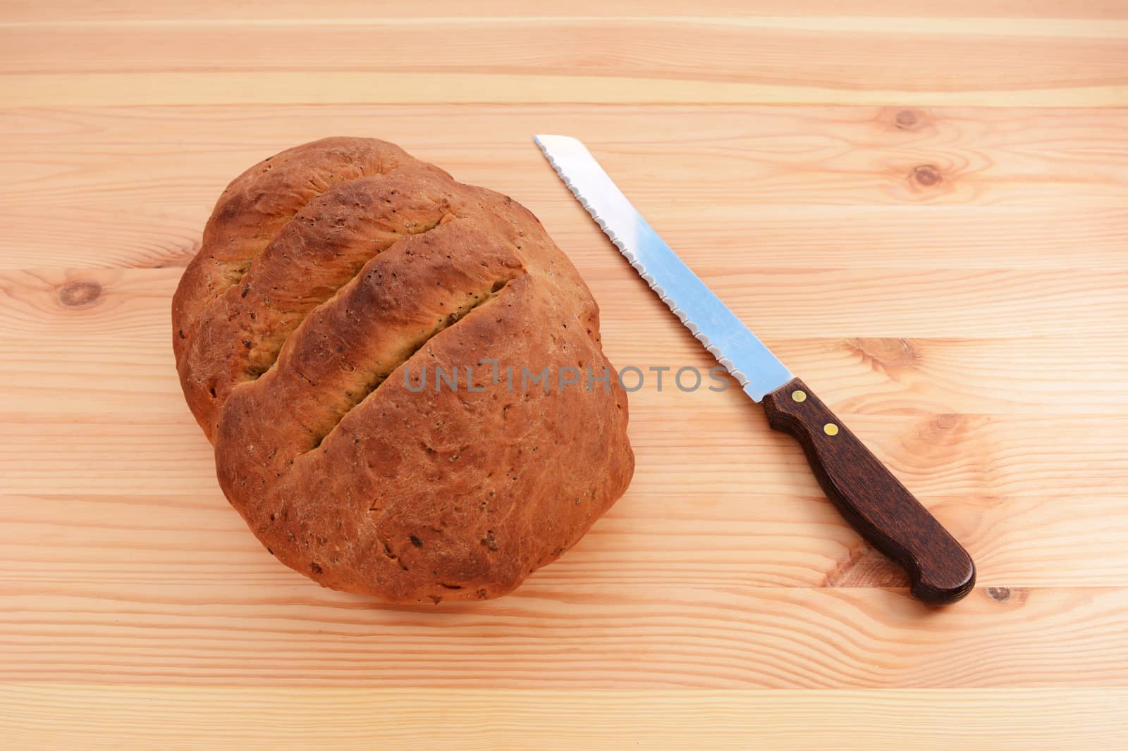 Freshly baked seeded loaf with a bread knife on a wooden table 