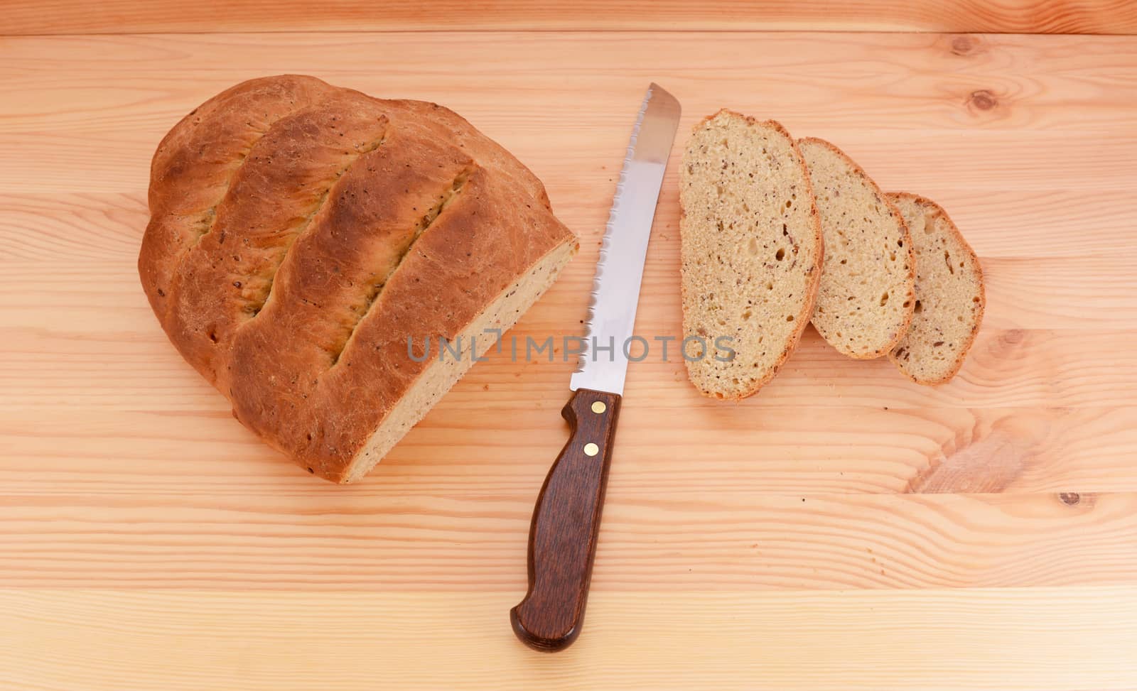 Fresh loaf of bread with a sharp knife and three cut slices on a pine table