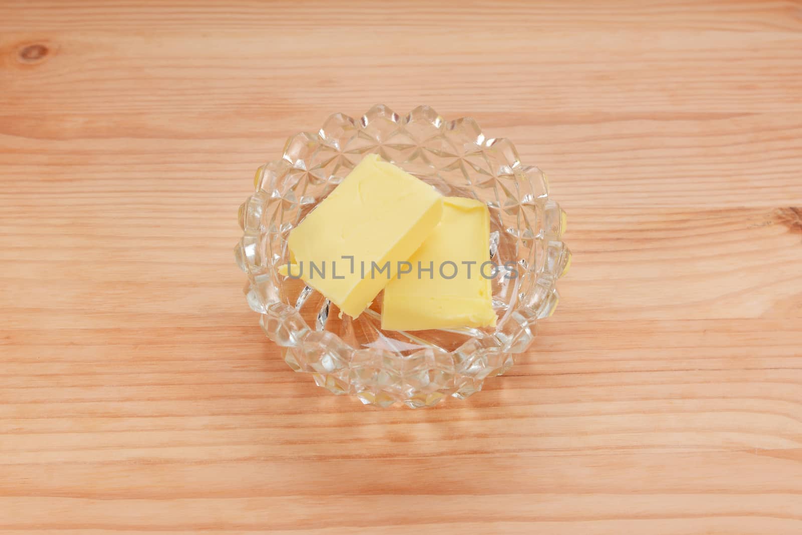 Two pats of butter in a glass dish on a wooden table