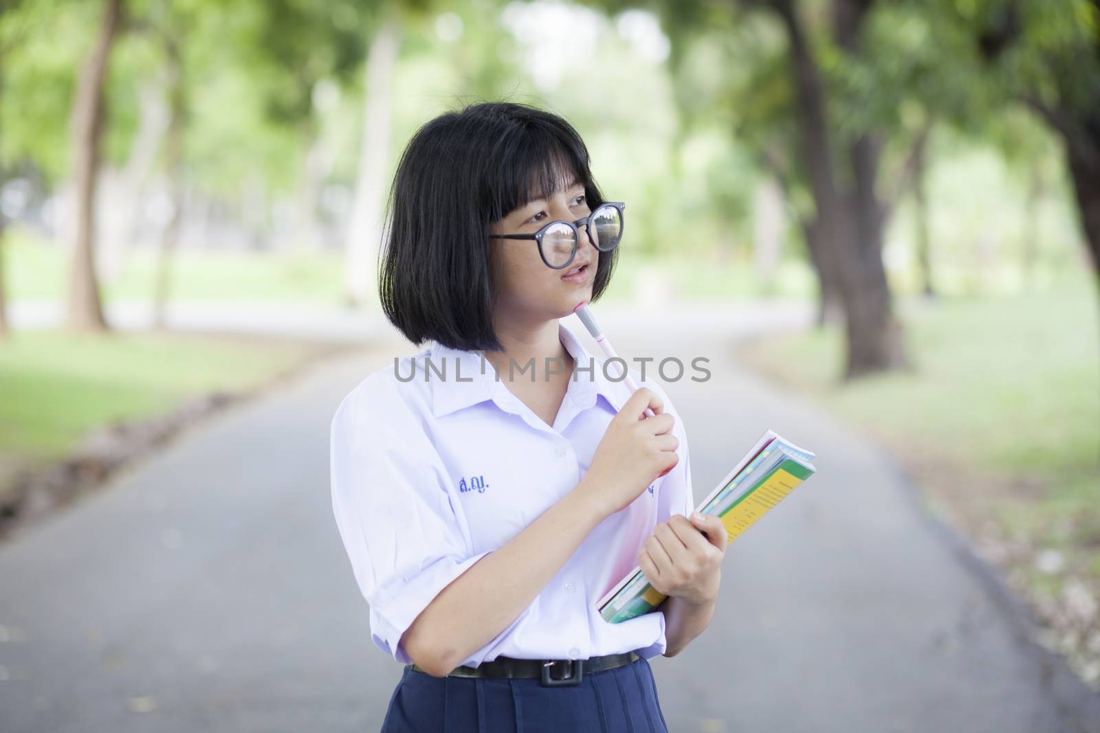 Schoolgirl standing holding a book. Relaxed, smiling and happy. In the park