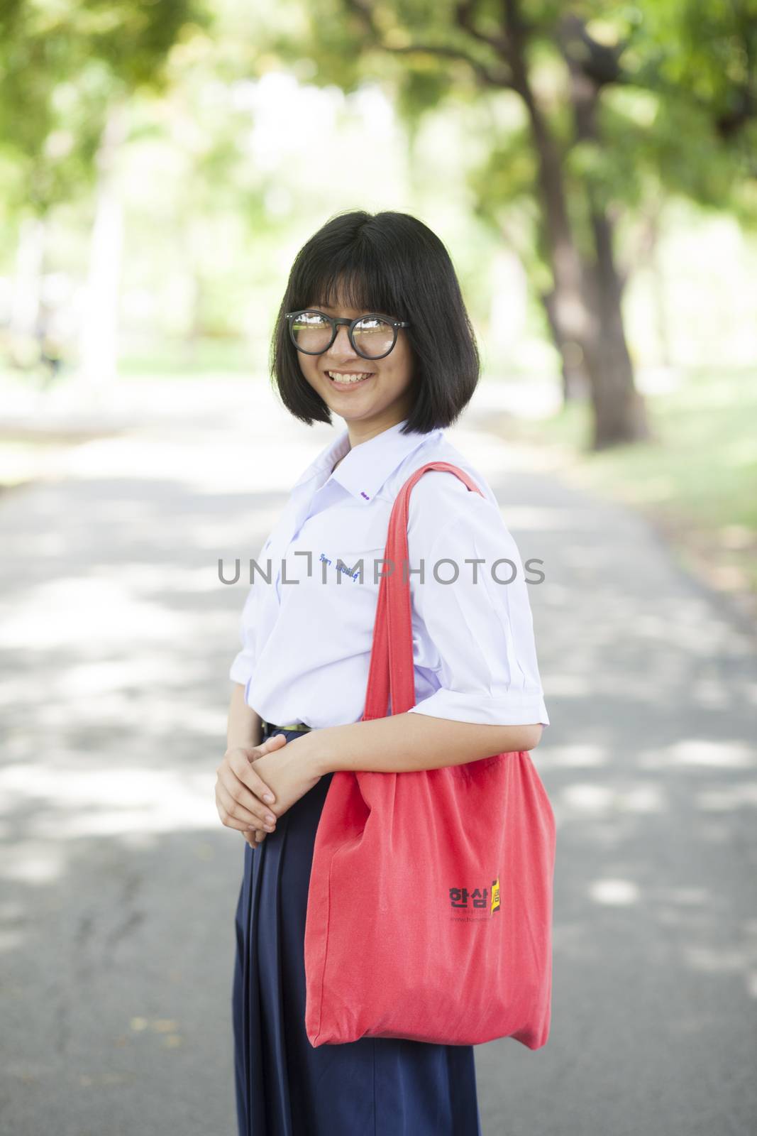 Female students. Red carrying bag Asian girl standing on a walkway in the park.
