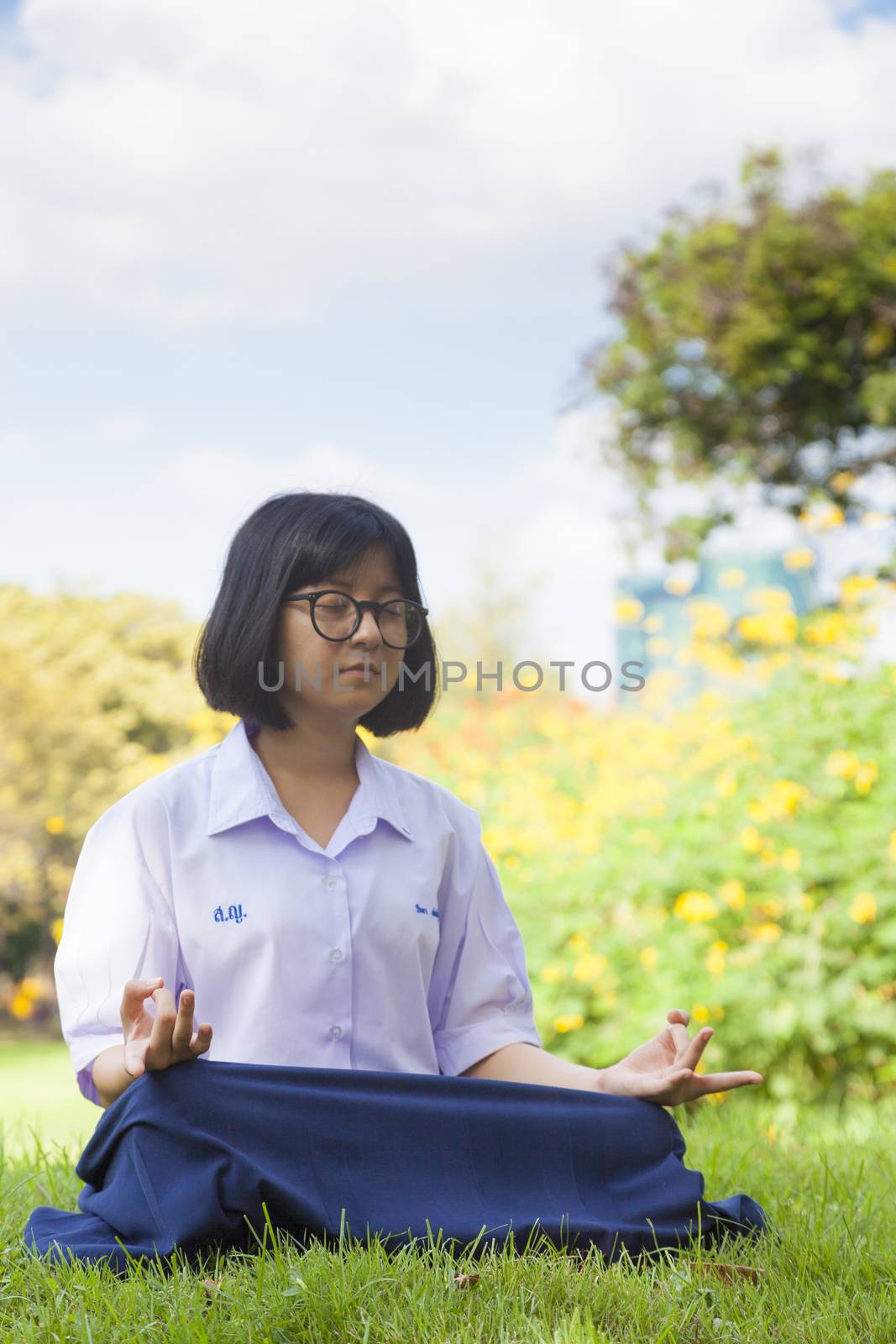 Schoolgirl are meditating. The grass in the park. Weather cloudy and clear sky.