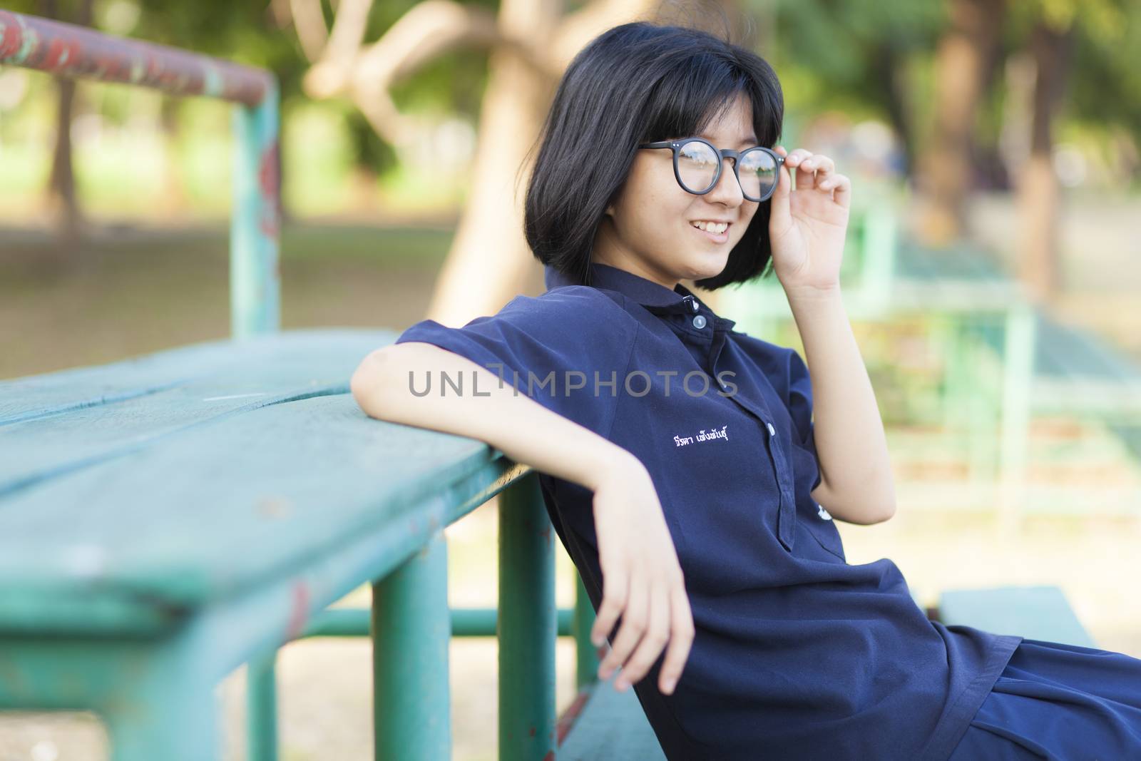 Girl wearing glasses sitting on the bench. Smiling a happy Within the park