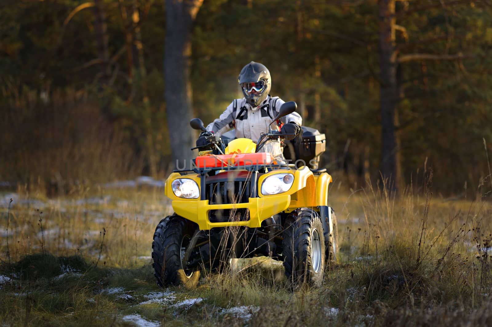 Horizontal portrait of a man in helmet and safety goggles looking into the camera while sitting on all-terrain vehicle against snowy late autumn landscape.
