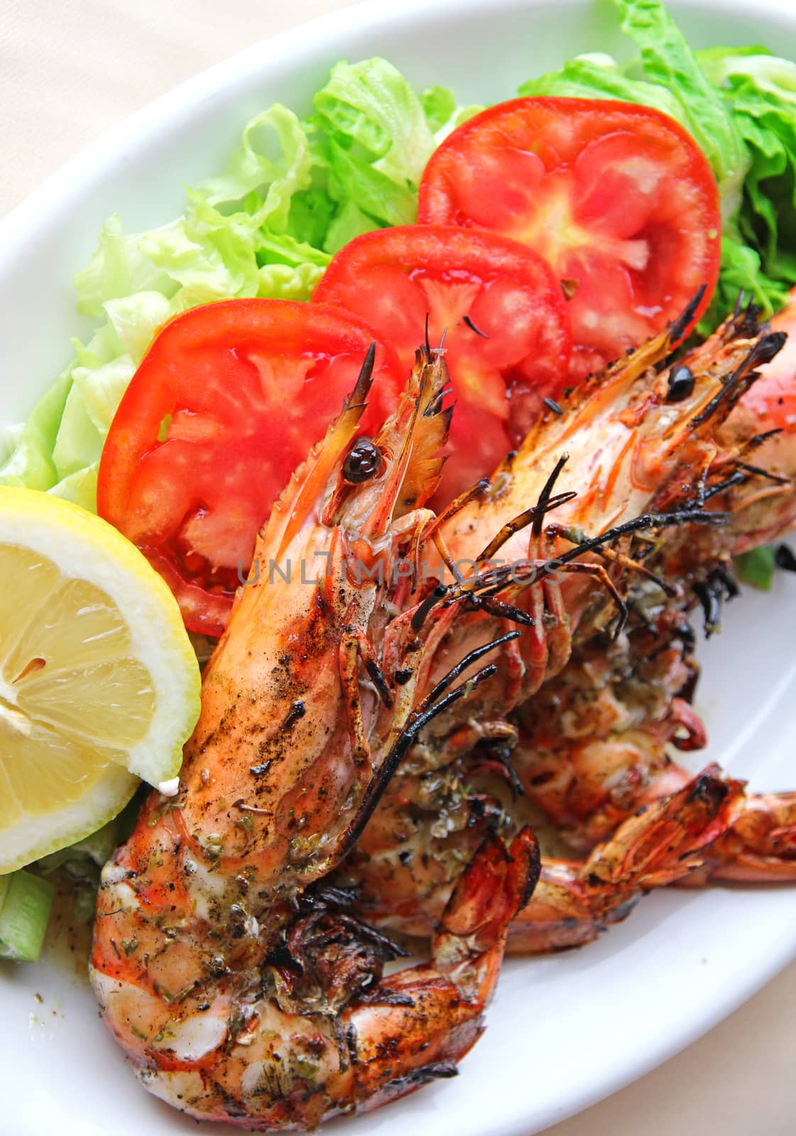 Fresh grilled shrimps with tomatoes, green salad and lemon on white plate 