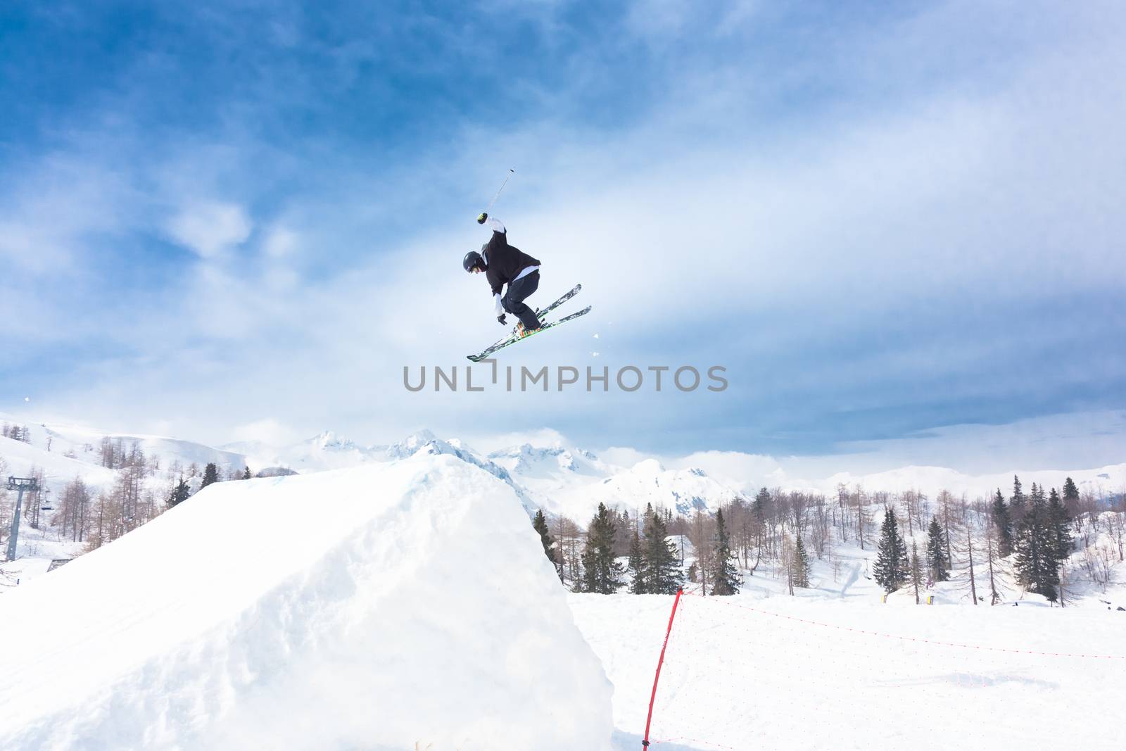 Free style skier performing a high jump. Ski lifts in the mountains in the background. 