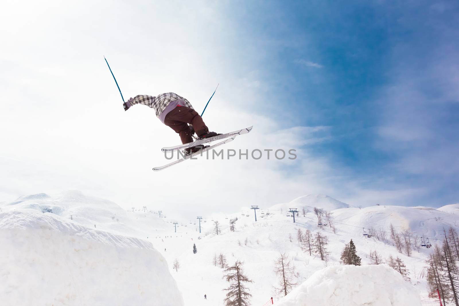Free style skier performing a high jump. Ski lifts in the mountains in the background. 
