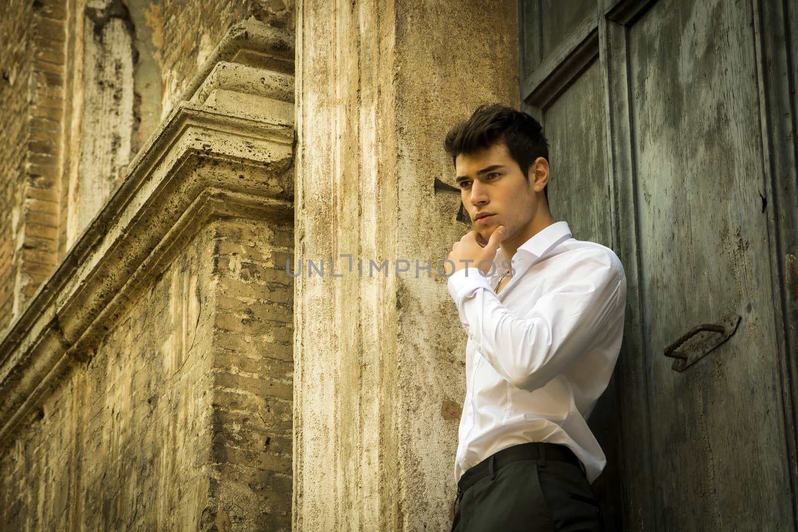 Elegant young man leaning against old wall and door, shot from below