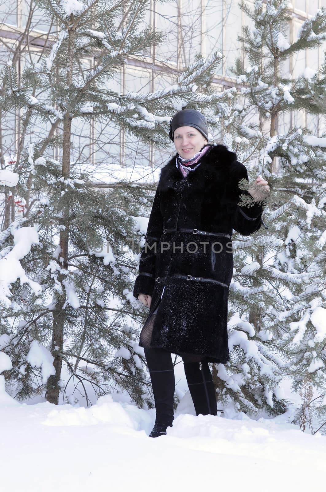 The cheerful woman in a black fur coat costs at snow-covered pines in park