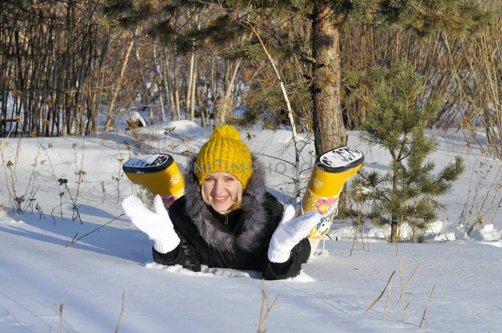 The joyful young woman lies on snow near a pine in park
