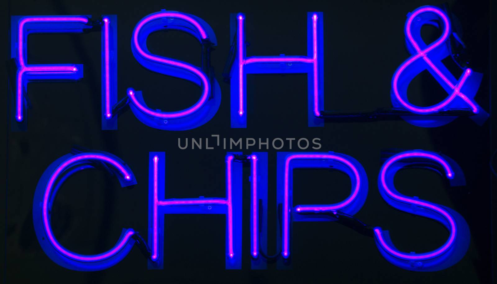 Fish and chips restaurant neon sign at night in street photo.