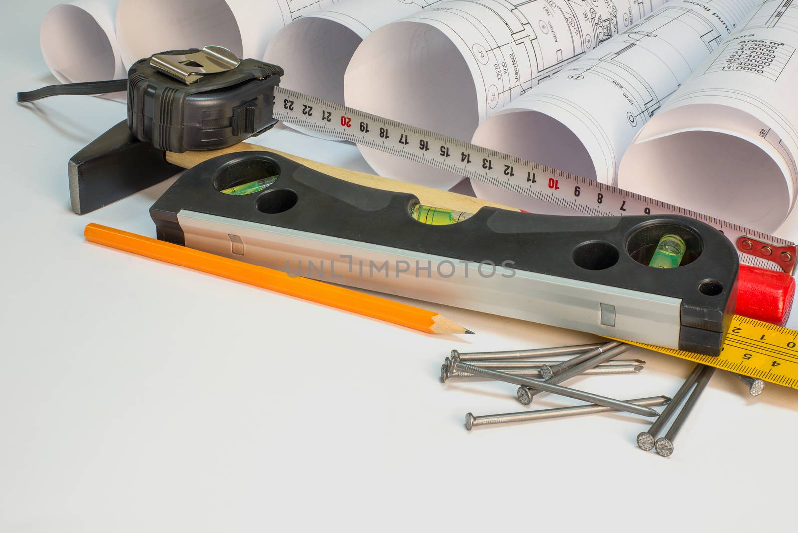 Drawing rolls, hammer, nails, builder's level, pencil, ruler and tape measure on white surface