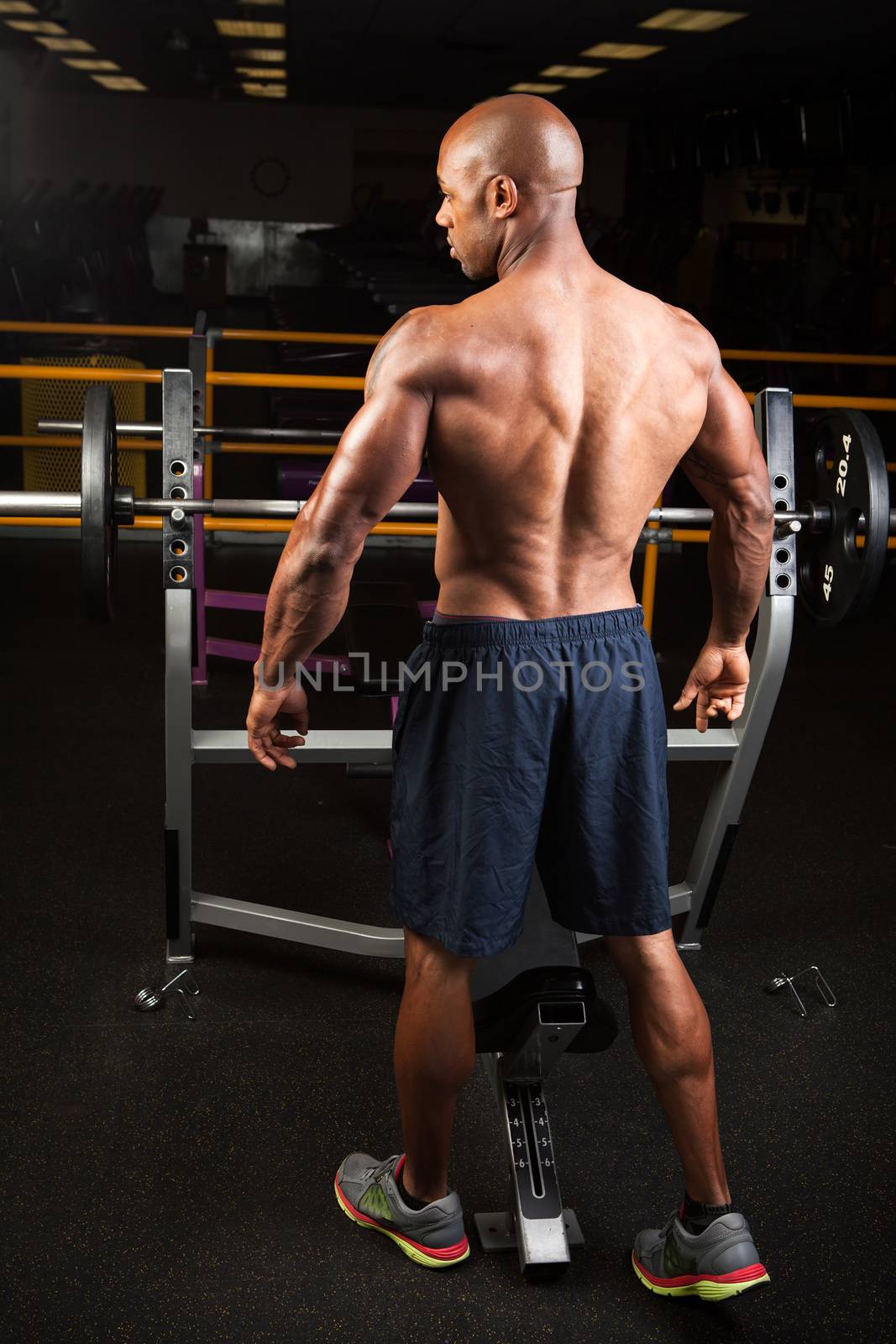 Toned and ripped lean muscle fitness man standing by a weight bench at the gym.